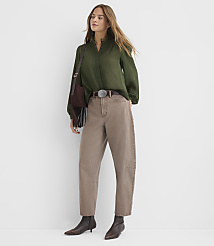 A woman in a green blouse and brown pants stands against a plain white background, accessorized with a brown belt, boots, and a fringed bag. carousel Product Image 3