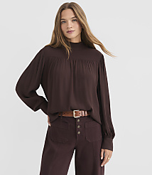 A woman in a brown mock-neck blouse and maroon pants stands against a plain white background. carousel Product Image 1