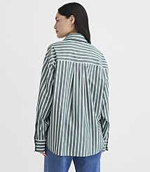 A woman in a green and white striped oversized shirt stands against a plain white background. carousel Product Image 4