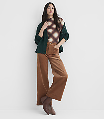 A woman in a patterned top, green cardigan, and brown corduroy pants stands against a plain white background. carousel Product Image 1