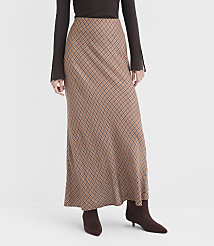 A person models a long, tan, checkered skirt with a brown top and boots against a plain white background. carousel Product Image 2