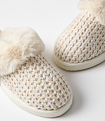 A pair of cozy, cream-colored knitted slippers with fluffy trim rests on a plain white background. carousel Product Image 2