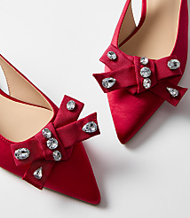 Two red satin pointed-toe heels with jeweled bows are displayed against a plain white background. carousel Product Image 2