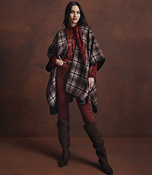 A woman in a plaid poncho and rust-colored pants stands against a textured brown background. carousel Product Image 4