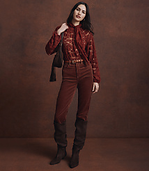 A woman in a rust-colored lace top and corduroy pants stands against a textured brown background. carousel Product Image 2