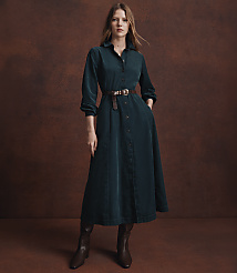 A woman in a teal corduroy dress and brown boots stands against a textured brown background. carousel Product Image 4