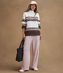 A woman in a fair isle sweater and pink pants stands with a black tote bag against a plain brown background. carousel Product Image 3