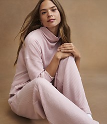 A young woman in a pink waffle-knit loungewear set sits against a warm, neutral background. carousel Product Image 2