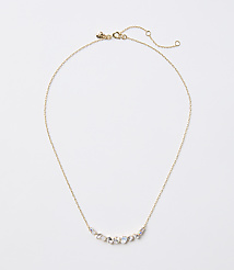 A delicate gold necklace with a curved arrangement of small, iridescent stones rests on a plain white background. carousel Product Image 1