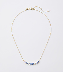 A delicate gold necklace with a curved arrangement of blue and white gemstones rests on a plain white background. carousel Product Image 1
