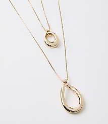 Two gold necklaces with abstract pendant shapes are layered against a plain white background. carousel Product Image 2