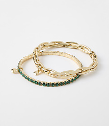Two gold bracelets, one with a chunky chain design and the other adorned with green gemstones, rest on a plain white background. carousel Product Image 1