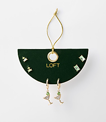 A set of green jeweled earrings, including martini glass and stud styles, are displayed on a dark green card with a gold loop and string against a plain white background. carousel Product Image 1
