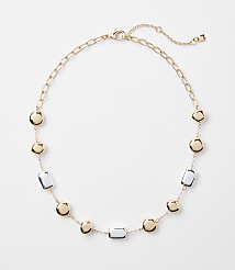 A gold chain necklace with alternating gold discs and clear rectangular beads is laid out on a plain white background. carousel Product Image 1