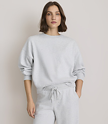 A woman in a grey sweatshirt and sweatpants stands against a plain, light grey background.