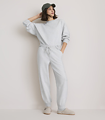 A woman in a light gray sweatsuit and a green baseball cap stands against a plain white background. carousel Product Image 1