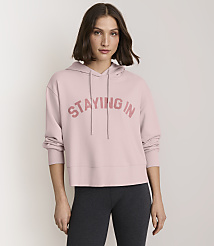 A woman in a pink "STAYING IN" hoodie and dark leggings stands against a plain white background. carousel Product Image 2