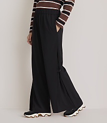 A person wearing black wide-leg pants with a striped shirt and sneakers stands against a plain gray background. carousel Product Image 2
