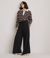 A woman in a striped rugby shirt and wide-leg black pants stands against a plain, light-colored wall. carousel Product Image 1