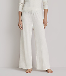 A person stands wearing cream-colored, wide-leg pajama pants with a subtle pattern against a plain, light gray background. carousel Product Image 2