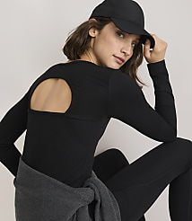 A woman in a black long-sleeved top with a cutout back and a baseball cap poses against a plain, light-colored background. carousel Product Image 1
