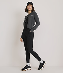 A woman in a dark outfit and baseball cap stands against a plain white background. carousel Product Image 1