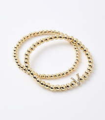 Two gold beaded bracelets, one with a diamond-encrusted "V" charm, rest on a plain white background. carousel Product Image 1