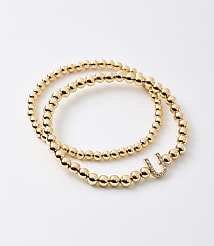 Two gold beaded bracelets, one with a diamond-encrusted "U" charm, lie on a plain white background. carousel Product Image 1