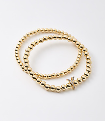 Two gold beaded bracelets, one with a diamond-studded "X" charm, are arranged on a plain white background. carousel Product Image 1