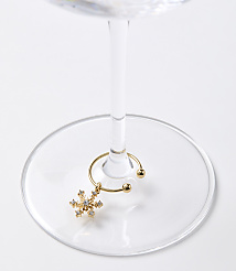 A gold snowflake charm hangs from a wine glass stem, resting on a clear glass base against a white background. carousel Product Image 2