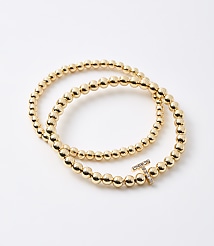 Two gold beaded bracelets, one with a diamond-encrusted "T" charm, lie on a plain white background. carousel Product Image 1