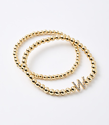 Two gold beaded bracelets, one with a diamond-encrusted "W" charm, rest on a plain white background. carousel Product Image 1
