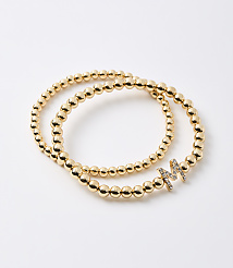 Two gold beaded bracelets, one with a diamond-encrusted letter "M" charm, rest on a plain white background. carousel Product Image 1