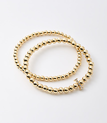 Two gold beaded bracelets, one with a diamond-encrusted "X" charm, are arranged on a plain white background. carousel Product Image 1