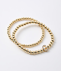 Two gold beaded bracelets, one with a diamond-encrusted infinity charm, lie on a plain white background. carousel Product Image 1