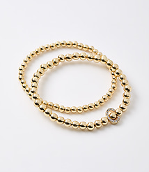 A gold beaded bracelet with a clover-shaped charm rests on a plain white background. carousel Product Image 1