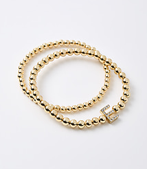 Two gold beaded bracelets, one with a diamond-encrusted letter "E" charm, lie on a plain white background. carousel Product Image 1