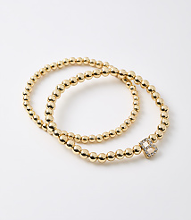 Two gold beaded bracelets, one with a diamond-encrusted letter "B" charm, lie on a plain white background. carousel Product Image 1