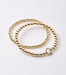 Two gold beaded bracelets, one with a diamond-encrusted "Q" charm, rest on a plain white background. carousel Product Image 1