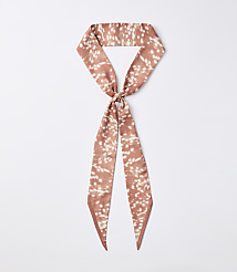 A rust-colored silky scarf with a white speckled pattern is knotted in the center, with its ends hanging down against a plain white background. carousel Product Image 1