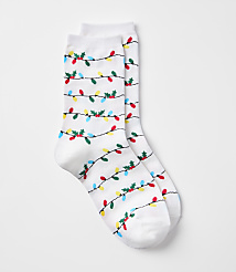 A pair of white socks with a pattern of colorful Christmas lights and holly adorns the foreground, set against a plain white background. carousel Product Image 1