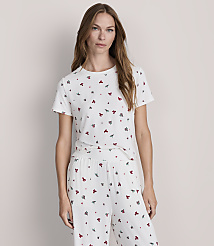 A woman in a white t-shirt and pants with a small floral pattern stands against a plain, light gray background. carousel Product Image 2