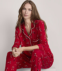 A woman in red pajamas with a bow pattern sits against a plain gray background. carousel Product Image 1