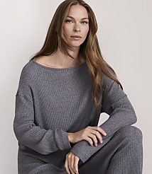 A woman in a grey ribbed sweater and pants poses against a plain, light background.