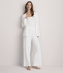 A woman in white pajamas stands against a plain, light-colored wall. carousel Product Image 2