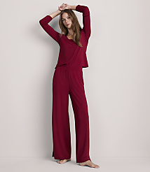 A woman in a burgundy pajama set with her arms raised stands against a plain, light gray background. carousel Product Image 1