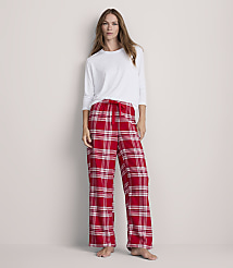 A woman stands in red plaid pajama bottoms and a white long-sleeved shirt against a plain, light-colored wall. carousel Product Image 1