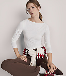 A woman in a white boatneck shirt and brown pants, with a patterned scarf draped around her waist, sits against a plain white background. carousel Product Image 1