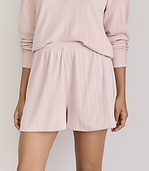 A person models a pink ribbed pajama set, with the shorts in the foreground and a plain background. carousel Product Image 2