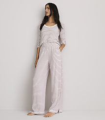 A woman in striped pajamas stands against a plain, light-colored wall.